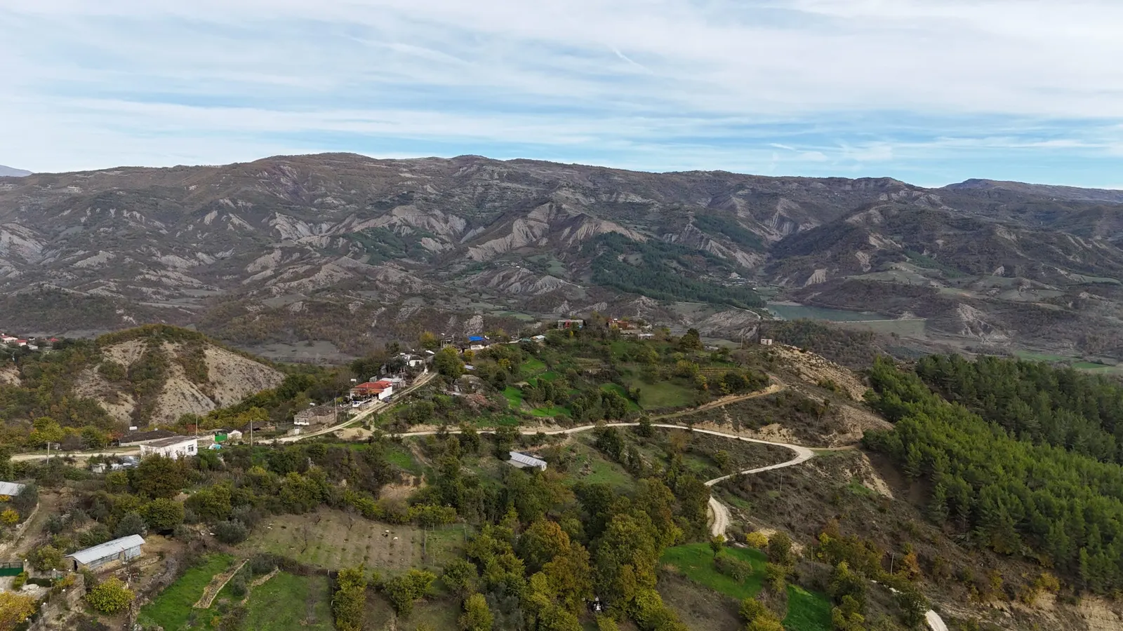Aerial view of Komarak village on a hillside below bare eroded mountains