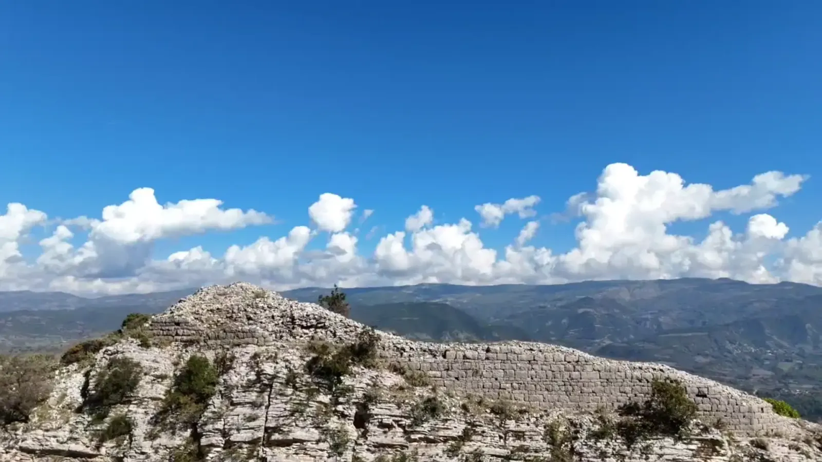Abschnitt der antiken illyrischen Burgmauer entlang eines felsigen Grats über Këlcyrë unter Wolken
