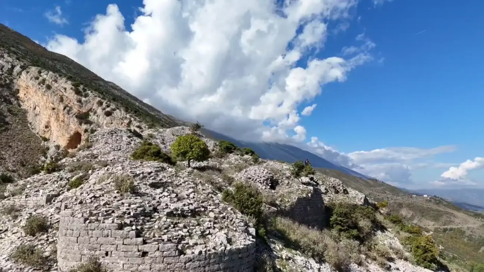 Gerundete illyrische Steinmauer auf einer Kalksteinkuppe mit Felsen und Bergen dahinter