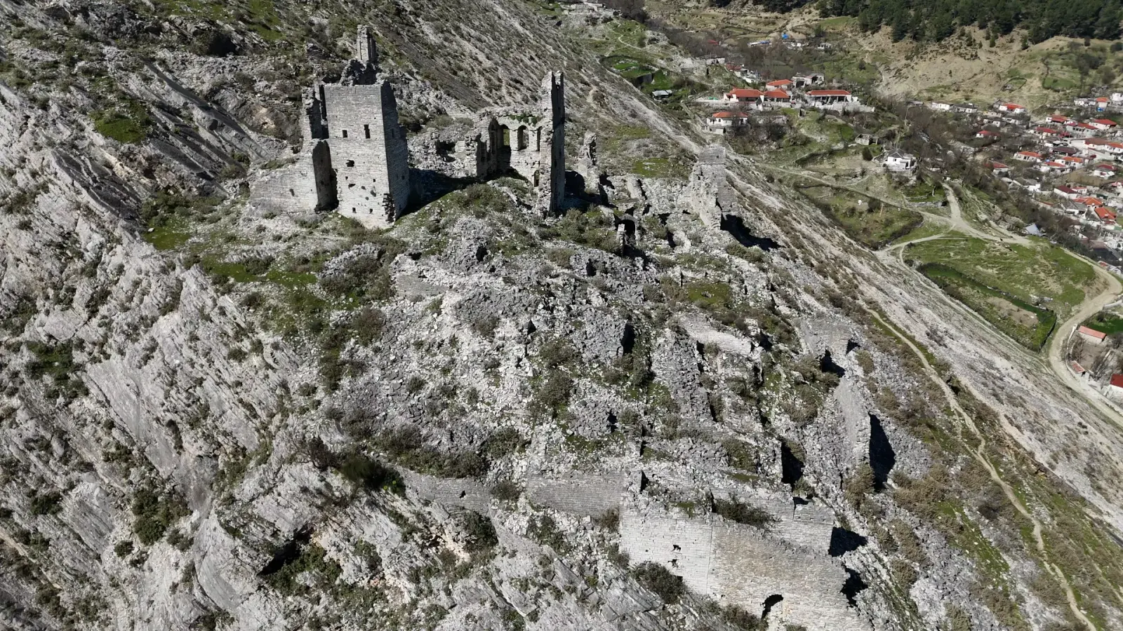 Torri in pietra in rovina su un pendio calcareo sopra i tetti rossi di Këlcyrë
