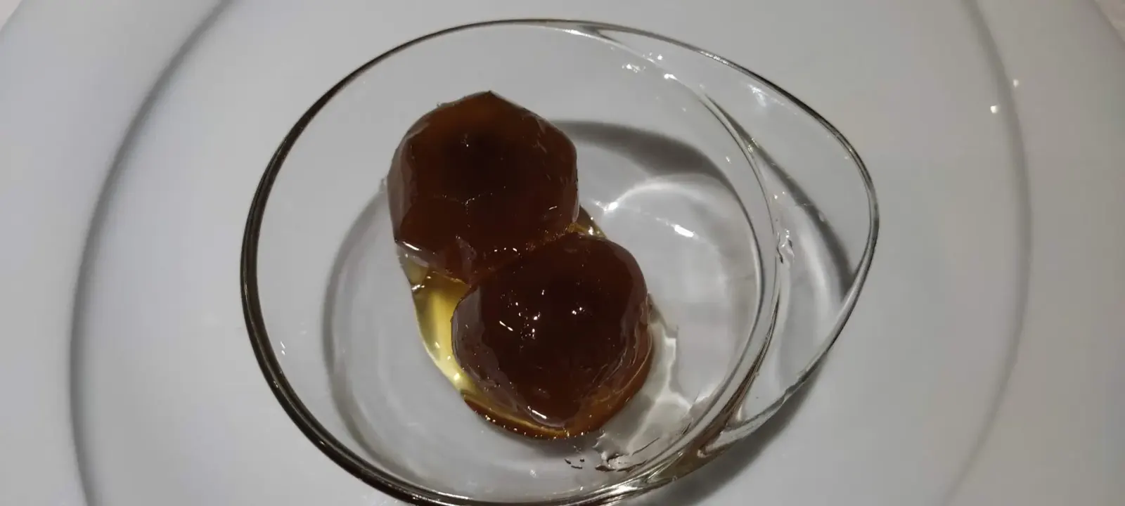 Zwei dunkle, in Sirup glasierte Löffelsüßigkeiten in einer kleinen Glasschale auf einem weißen Teller