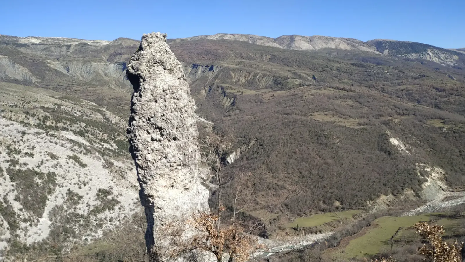 Der Menhir Guter Stein über einem weiten erodierten Tal und Bergkämmen