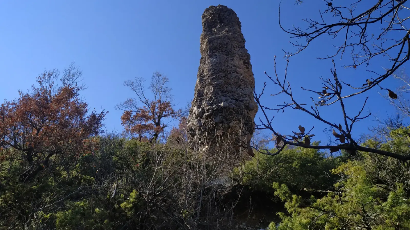 Der Menhir Guter Stein ragt vor blauem Himmel über Sträucher und herbstliche Bäume