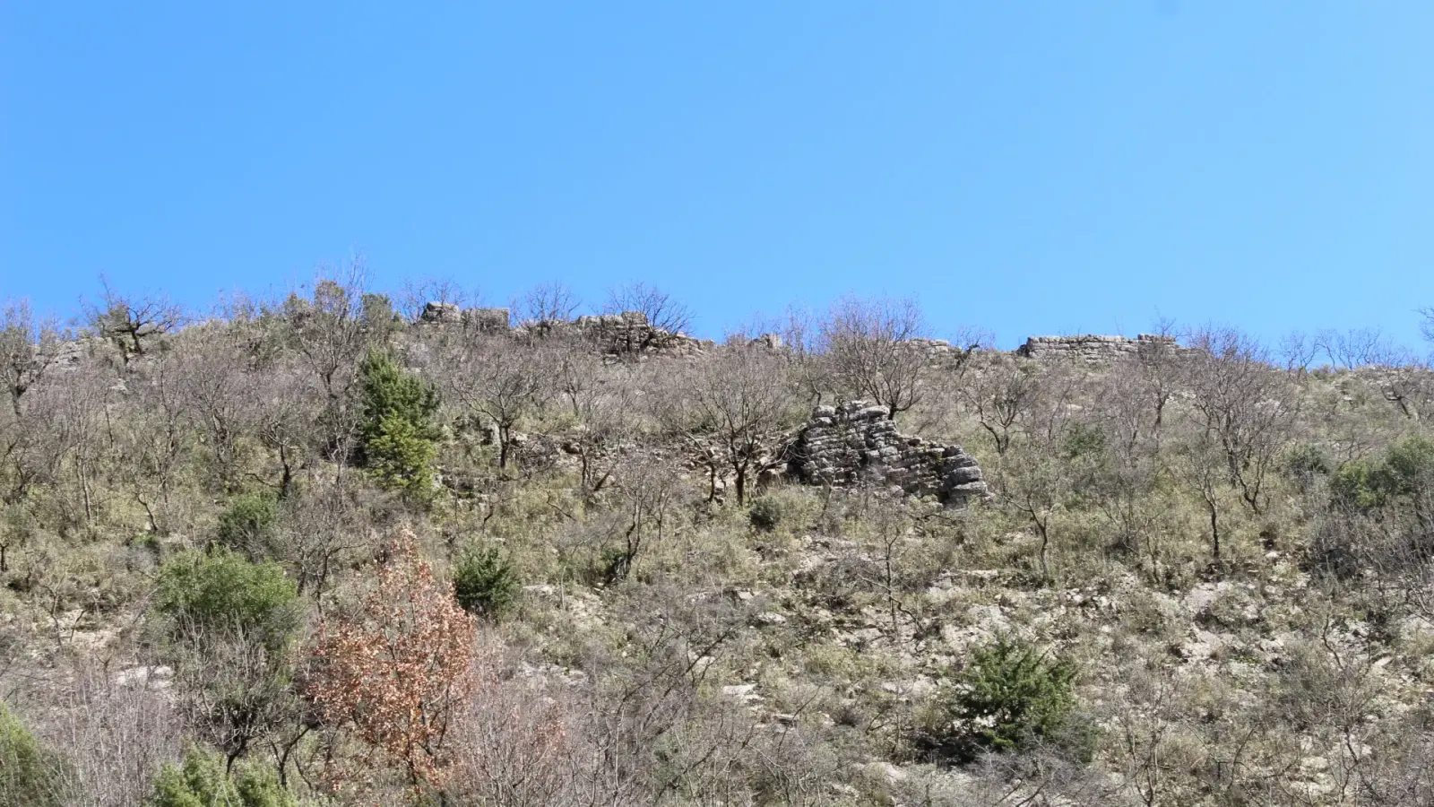 Reste der Festungsmauer auf einer buschigen Hügelkuppe über dem Dorf Kala