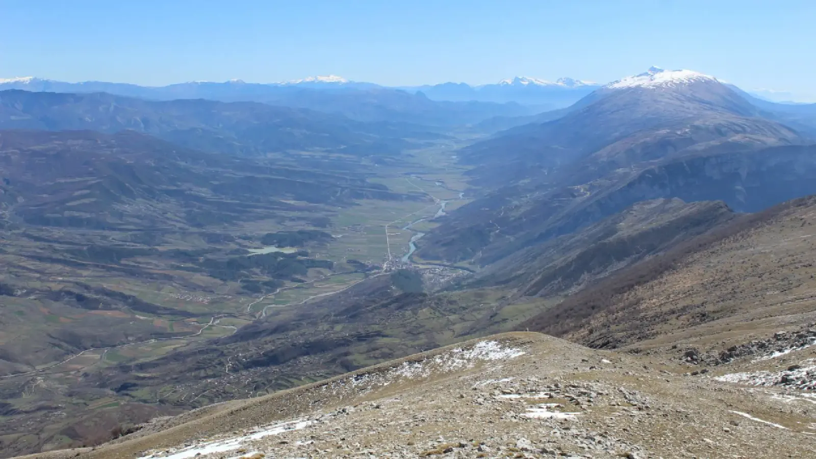 View from Mount Trebeshinë down a wide valley toward snow-capped peaks