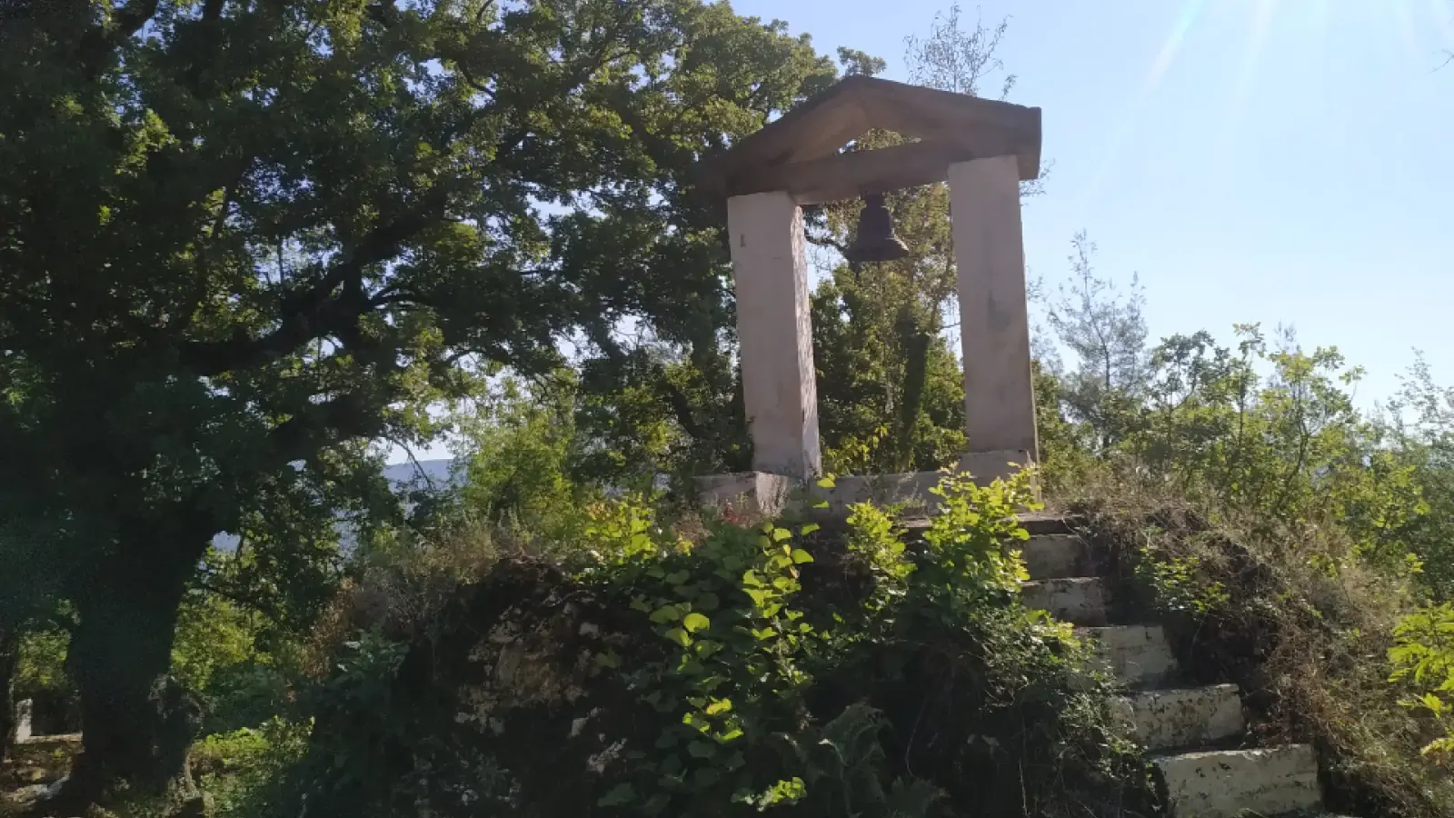 Stone steps leading up to the bell frame of Saint Mary's Church among trees in Mbrezhdan