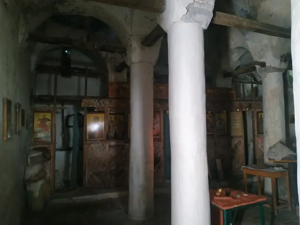 Dämmriger Innenraum der Nikolauskirche in Argovë mit hohen Säulen und gemalten Ikonen