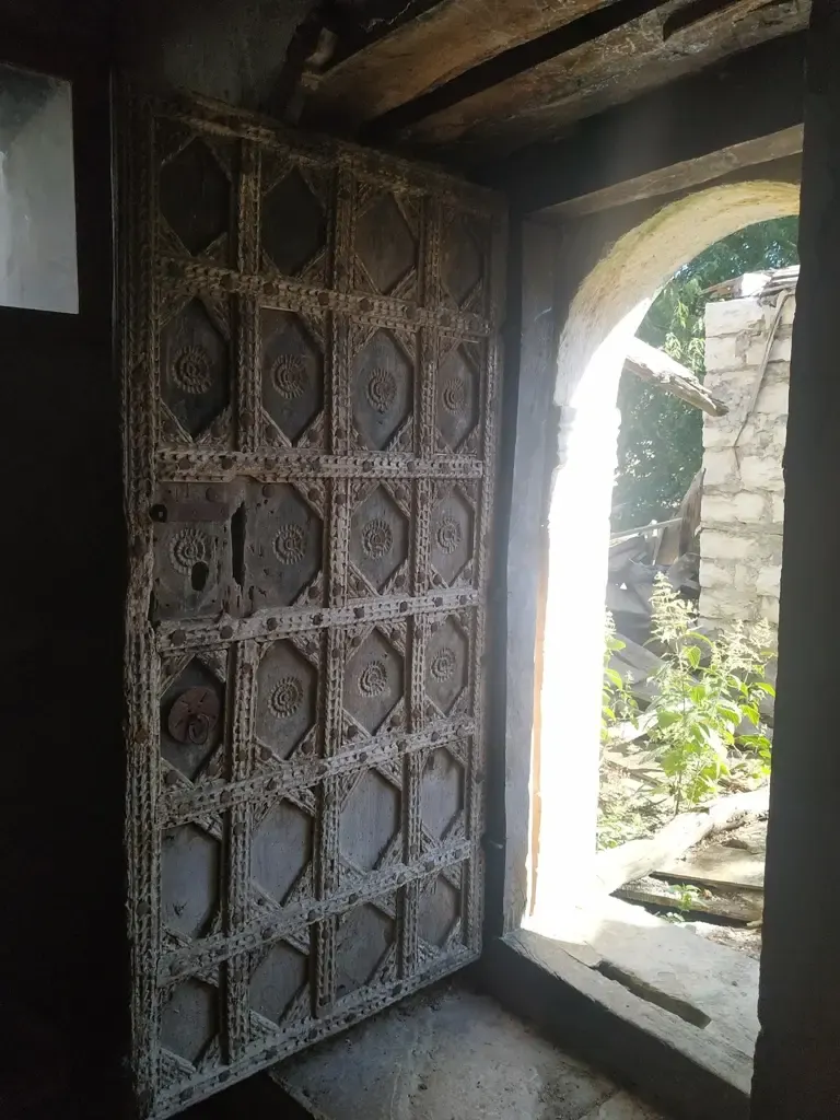 Schwere geschnitzte Holztür öffnet sich zu einer sonnigen Steinmauer an der Nikolauskirche, Argovë