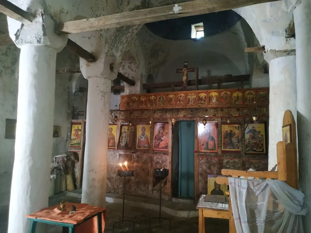 Kirchenschiff der Nikolauskirche in Argovë mit weißen Säulen, brennenden Kerzen und vergoldeter Ikonostase