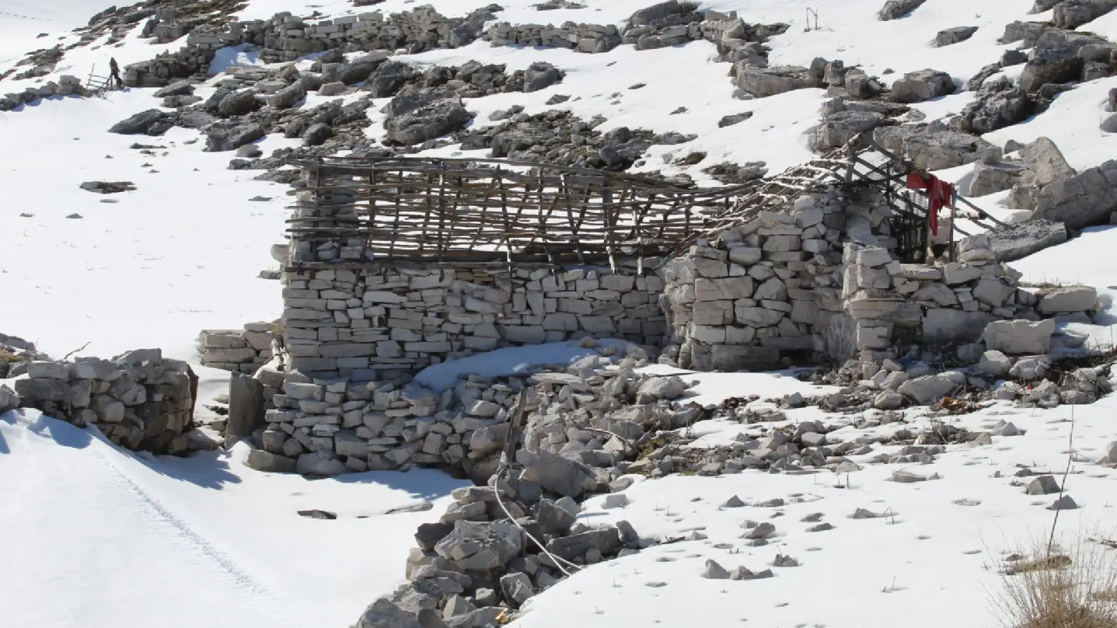 Dachlose Trockenstein-Hirtenhütte mit Holzgerüst zwischen Felsen und Schnee