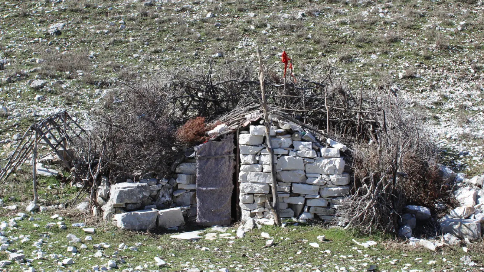 Niedrige Trockenstein-Hirtenhütte mit Zweigdach auf einer felsigen Bergweide