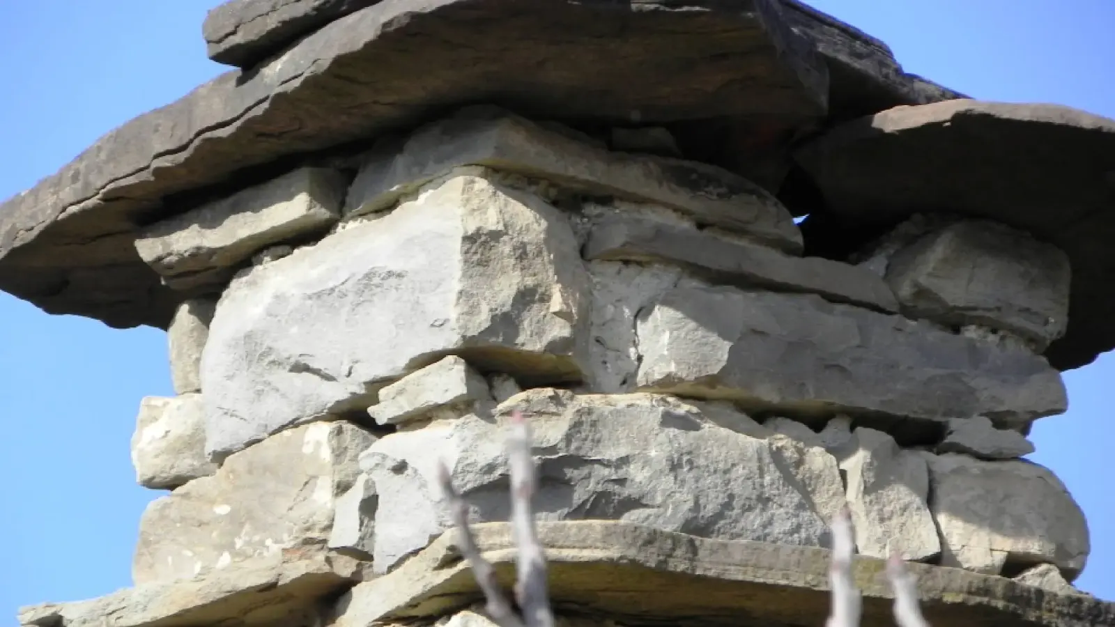 Nahaufnahme gestapelter flacher Steine auf einem traditionellen Schornstein vor blauem Himmel in Kenaj