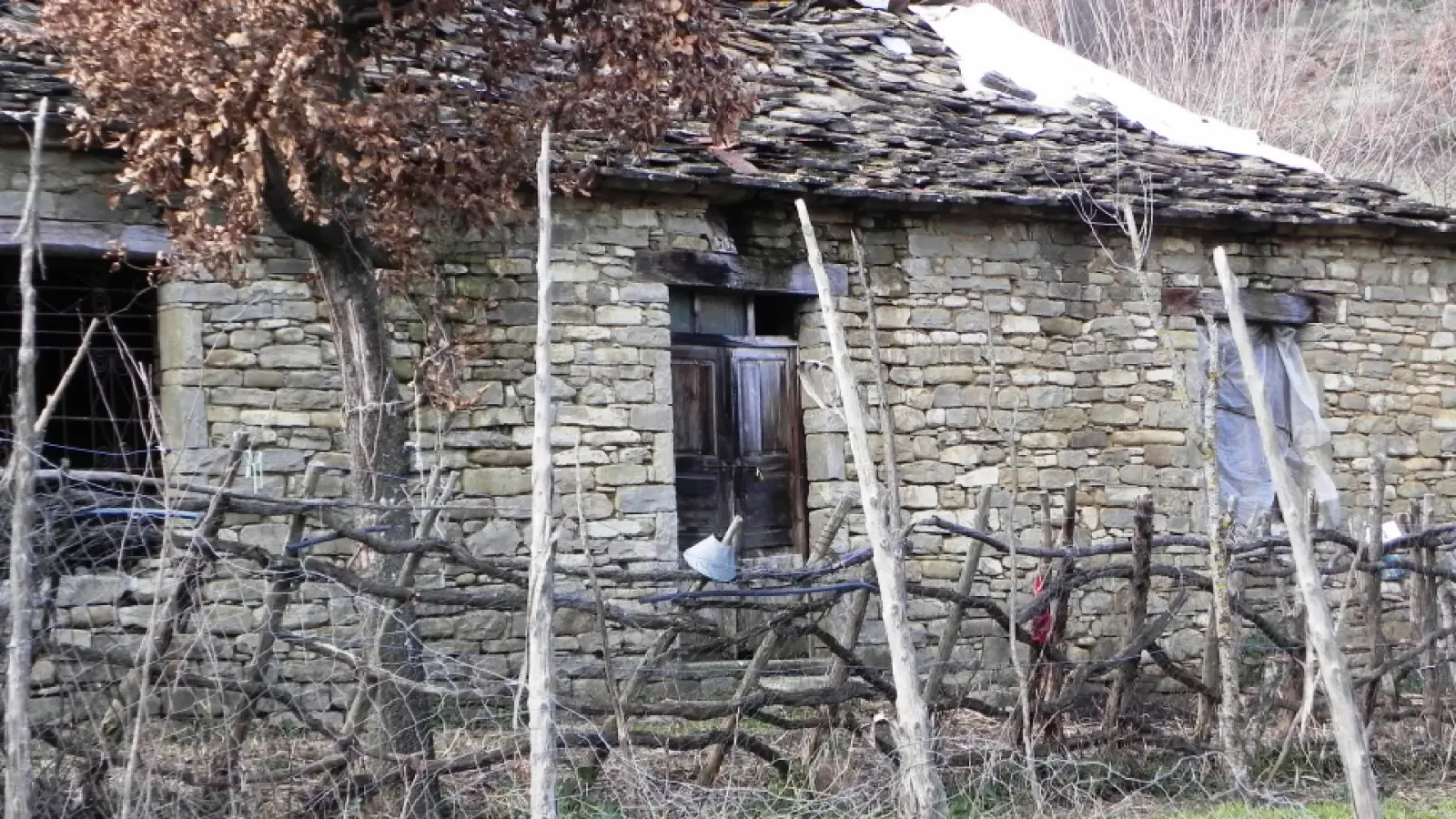 Altes Steinhaus mit Schieferdach hinter einem rustikalen Zweigzaun in Kenaj