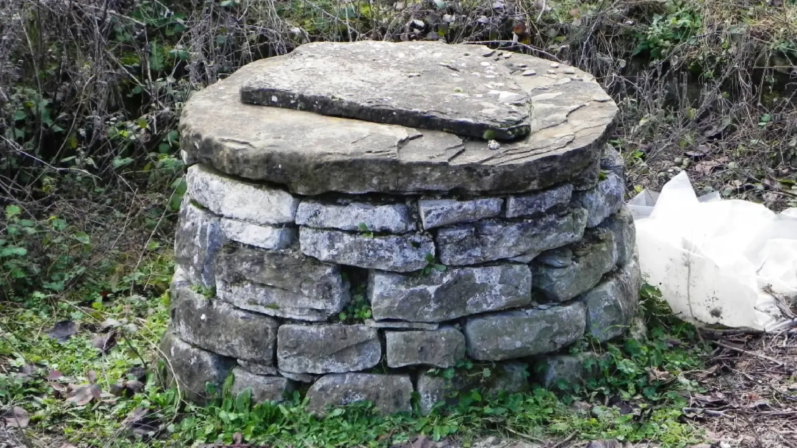 Runder Trockensteinbrunnen, mit einer flachen Steinplatte abgedeckt, im Dorf Kenaj