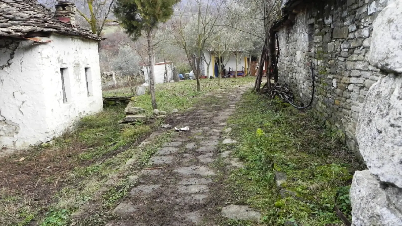 Steinplattenweg zwischen einem geweißten Haus und einer alten Steinmauer im Dorf Kenaj