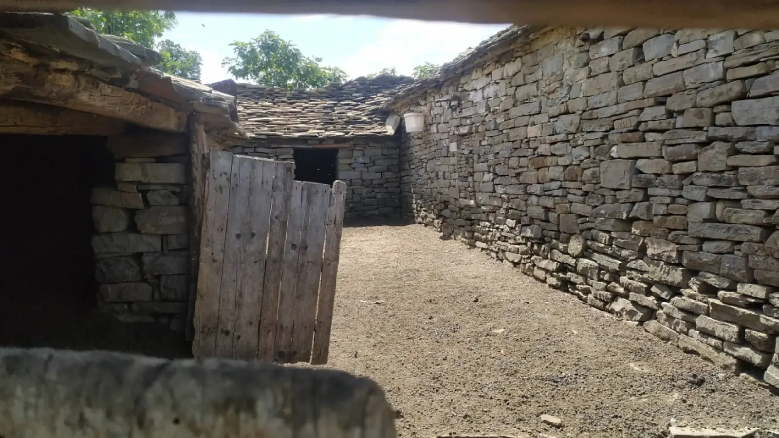 Cortile cintato in pietra con cancello di legno e tetti in lastre nel villaggio di Leskaj
