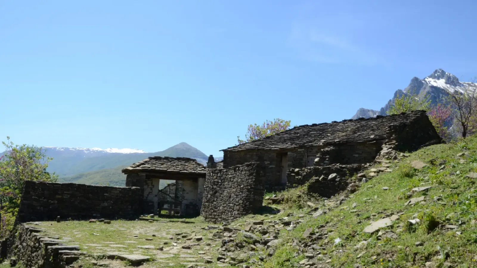 Alte Steinhäuser und ummauerter Hof im Dorf Limar unter verschneiten Gipfeln