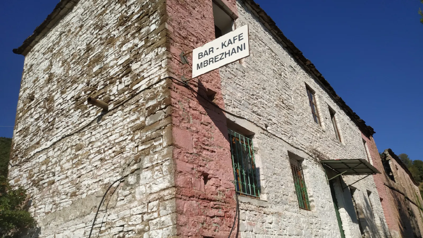 Alto edificio antiguo de piedra con un letrero de Bar-Kafe Mbrezhani en Mbrezhdan