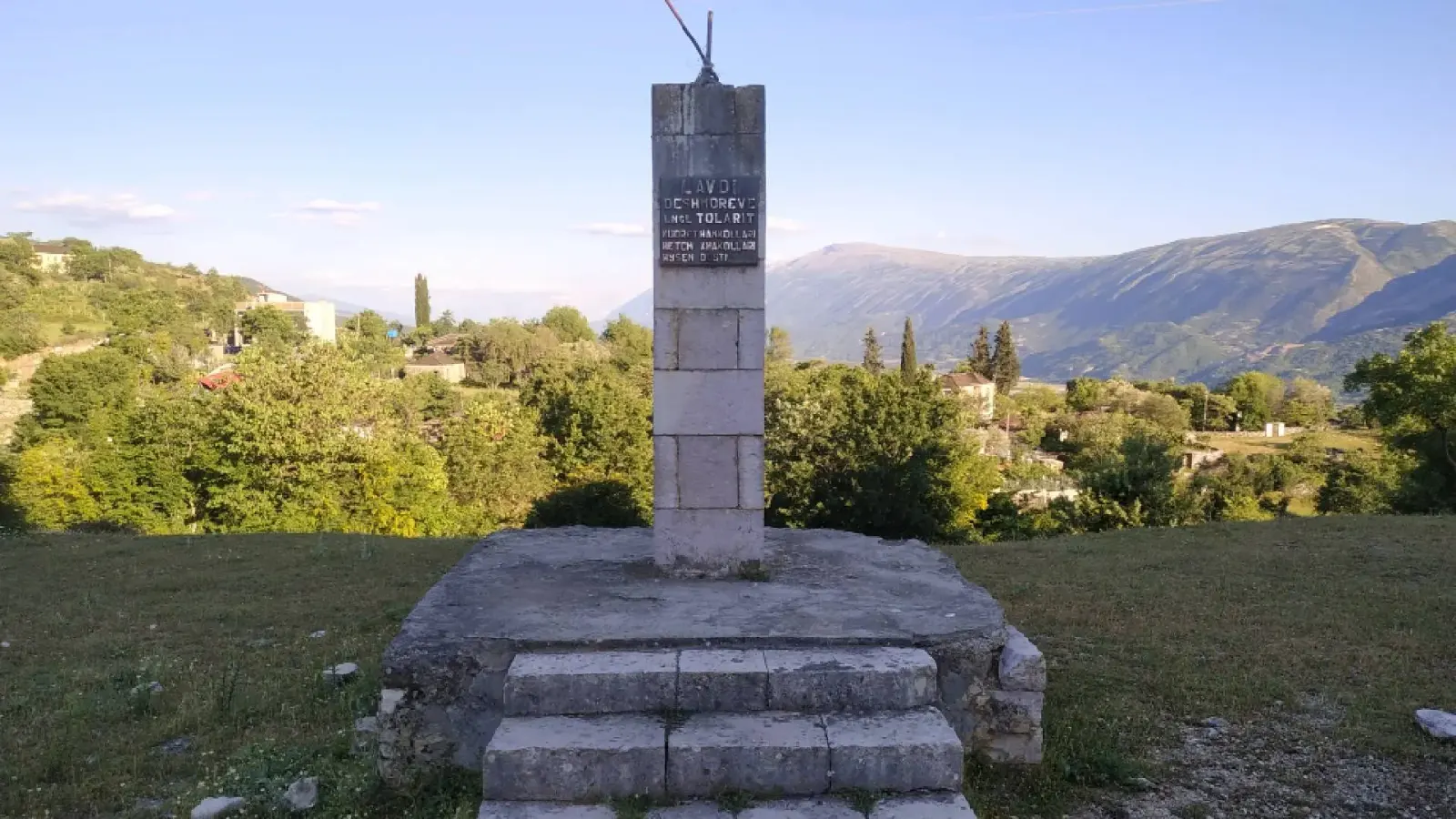 Obélisque commémoratif en pierre sur socle à gradins dominant les maisons de Tolar et des montagnes lointaines