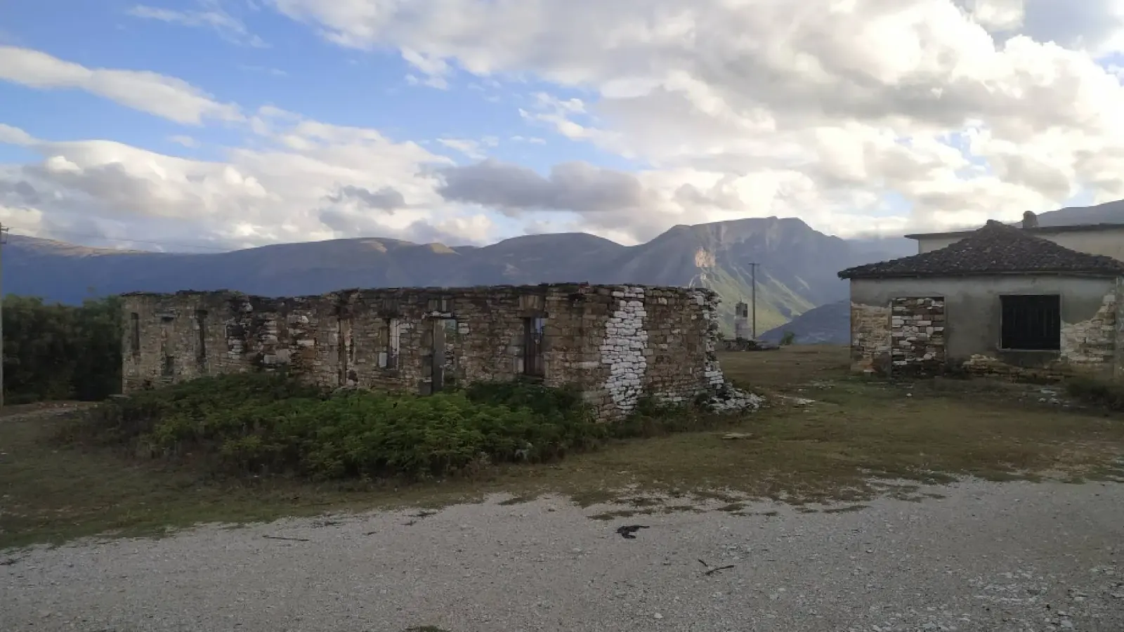 Ruine de pierre sans toit près d'une petite maison avec montagnes et nuages derrière, village de Tolar