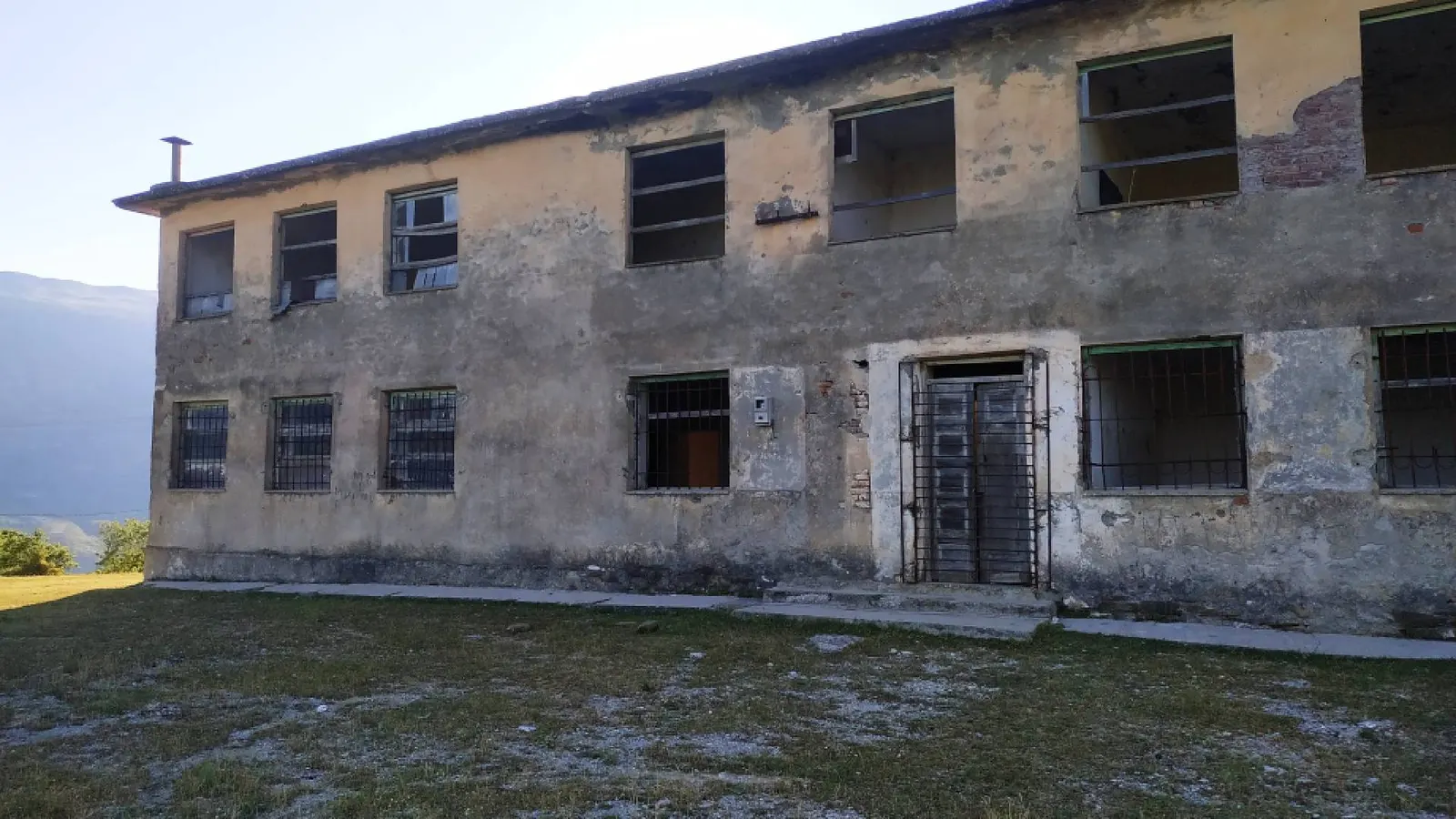 Bâtiment abandonné à deux niveaux aux fenêtres grillagées et à l'enduit écaillé dans le village de Tolar