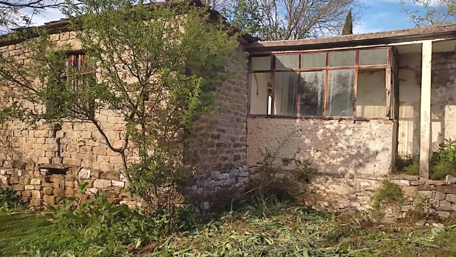 Maison en pierre avec véranda vitrée à demi cachée derrière un jeune arbre à Tolar