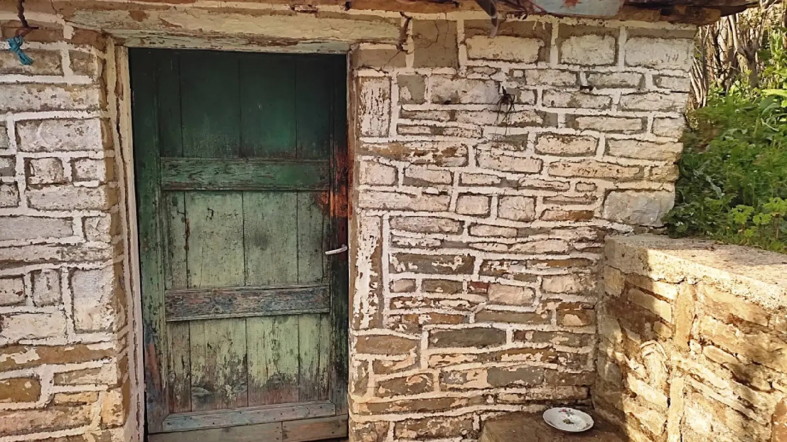 Porte en bois verte patinée dans un mur de pierre blanchi dans le village de Tolar