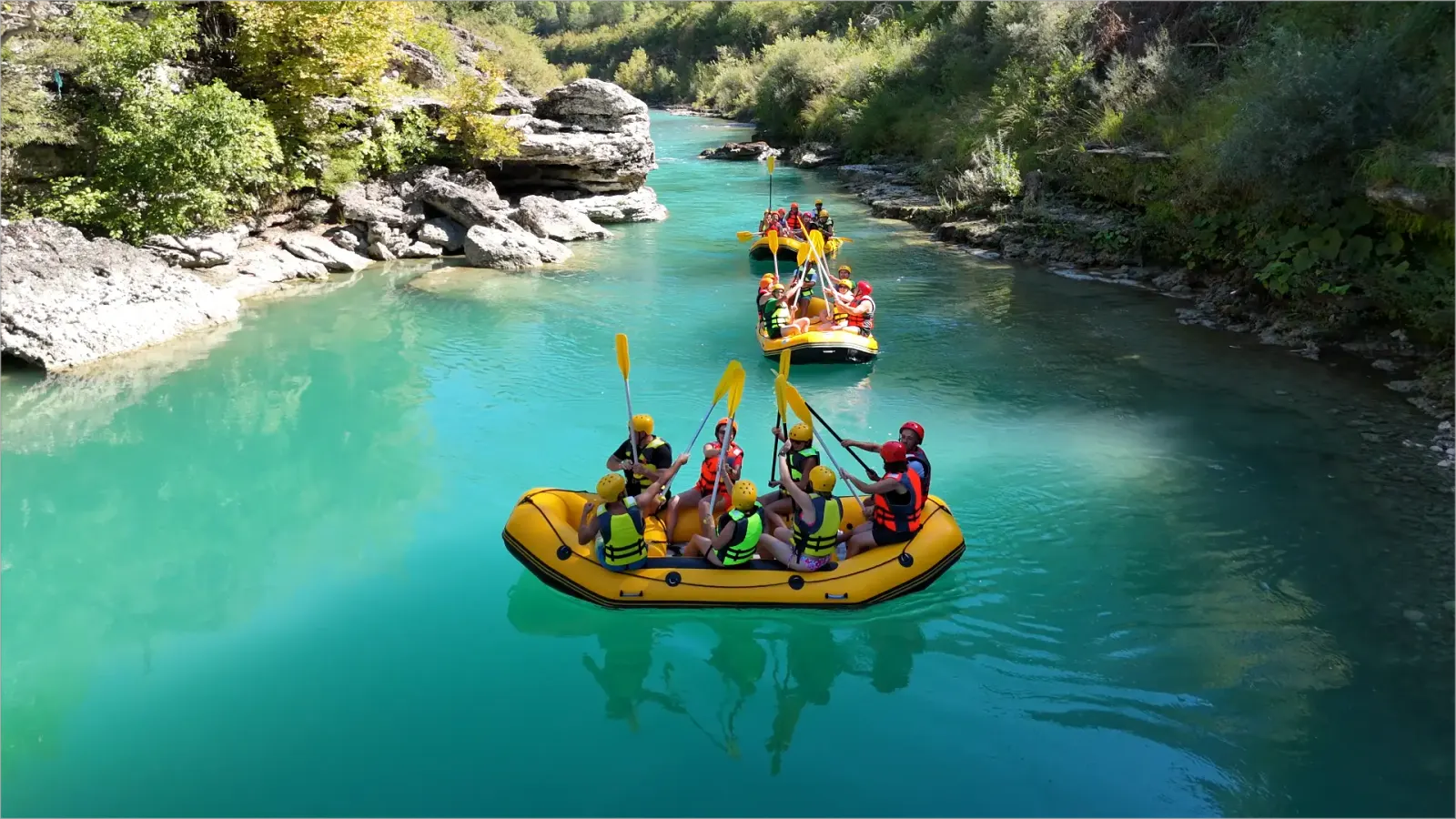 Aerial view of rafters in helmets paddling yellow rafts on the turquoise Vjosa River