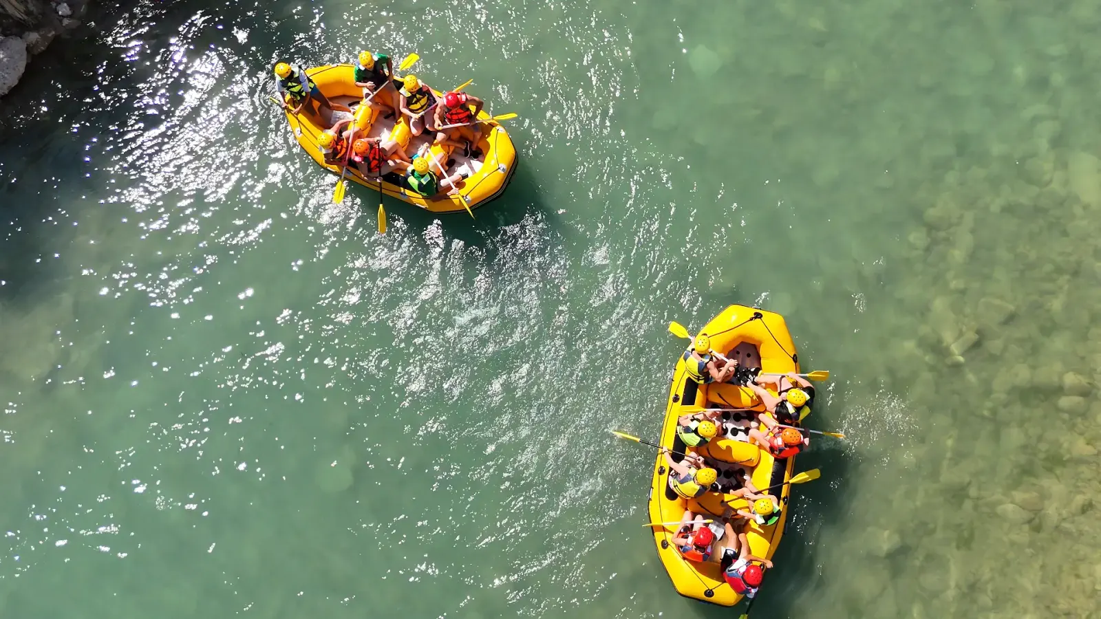 Overhead view of two yellow rafts full of paddlers on clear green water
