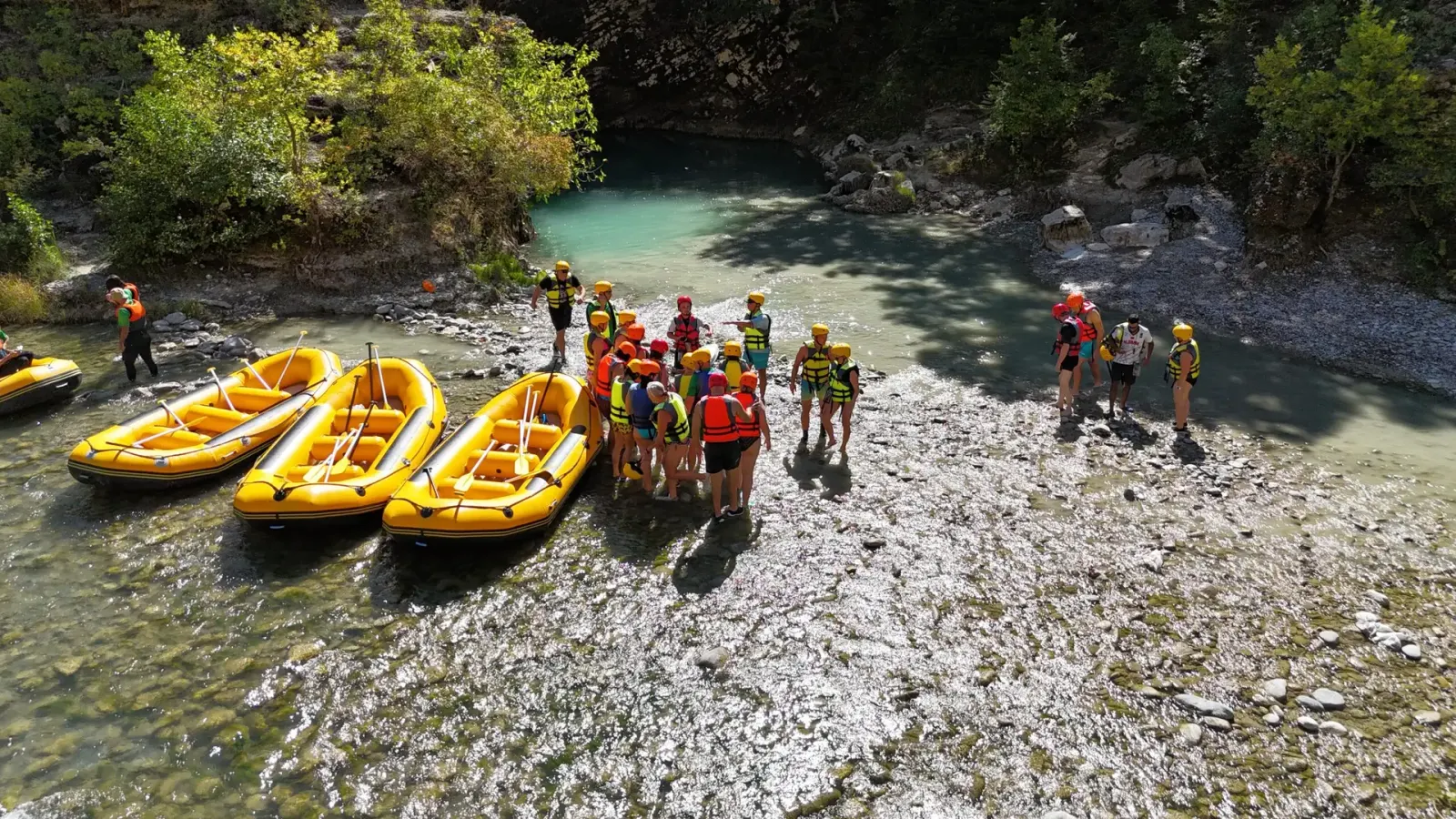Rafting group with helmets gathered beside yellow rafts on a gravel bank of the Vjosa