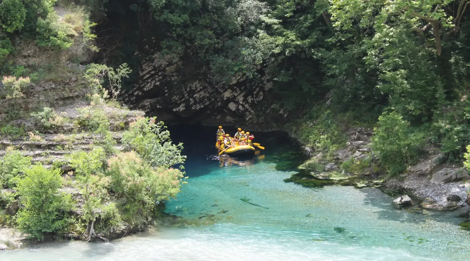 Yellow raft paddling out of a shaded cave into turquoise water on the Vjosa