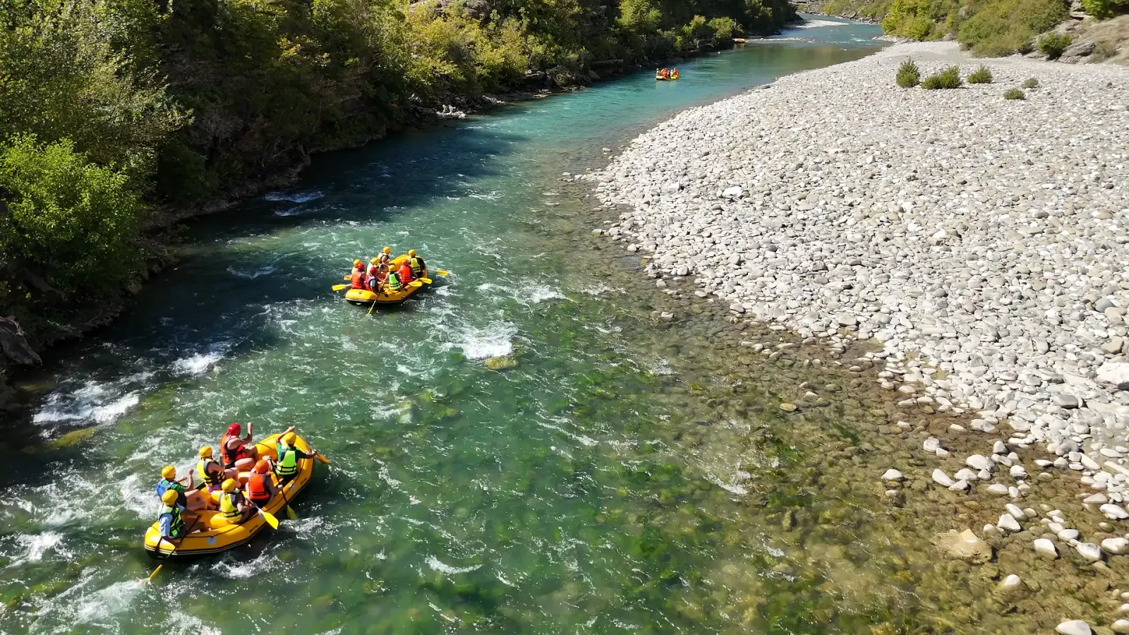 Rafts floating down a shallow stretch of the Vjosa River beside a wide gravel bar