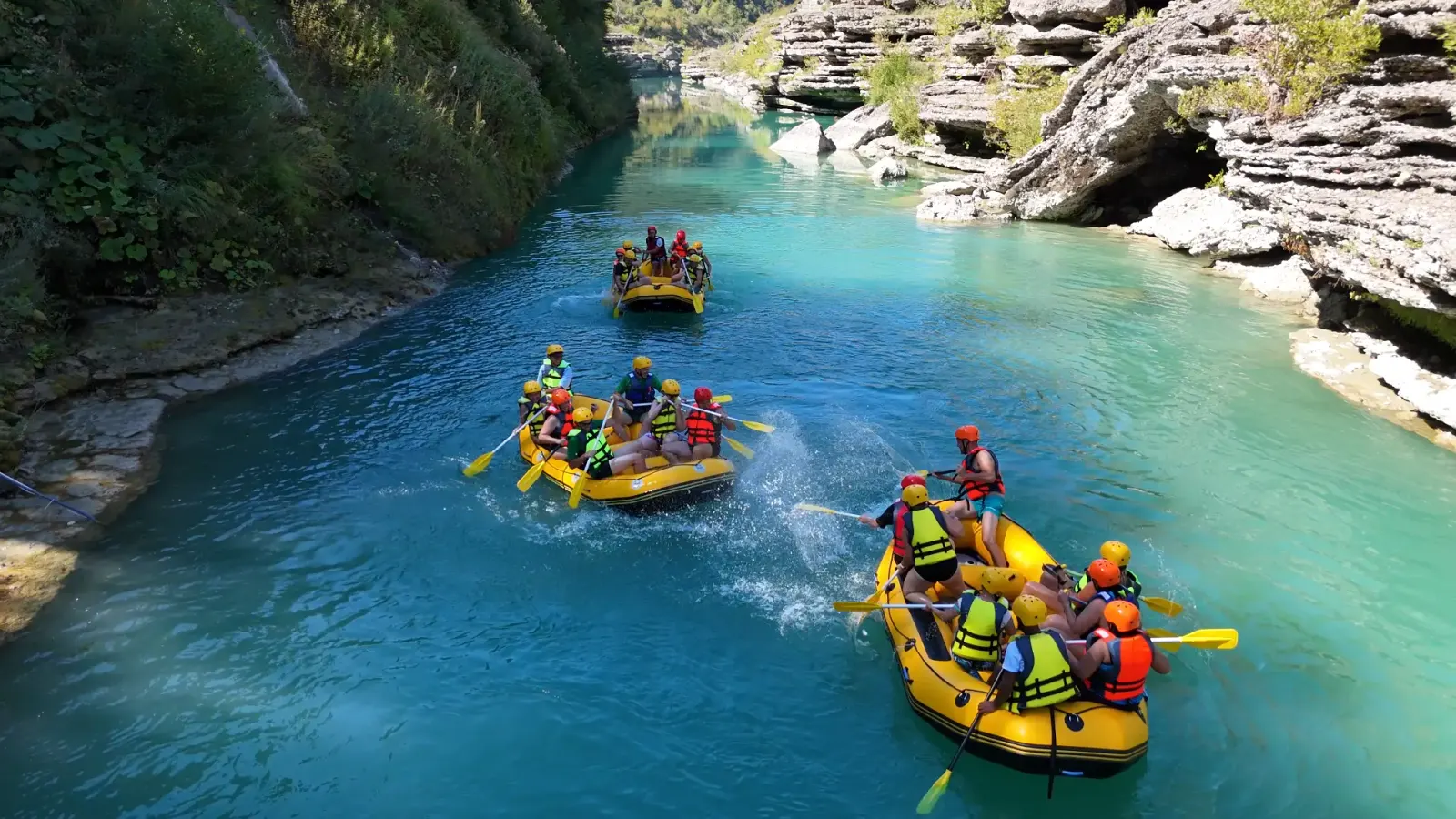 Rafters paddling yellow rafts through turquoise water between limestone cliffs of the Këlcyrë Gorge